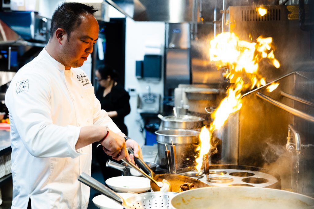 Photo of Chef Ethan Yang, Owner of Glass Box Del Mar in the kitchen cooking on a wok
