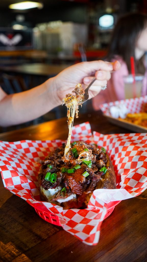 Photo of Abbey's Real Texas BBQ's brisket baked potato with cheese being pulled into the air