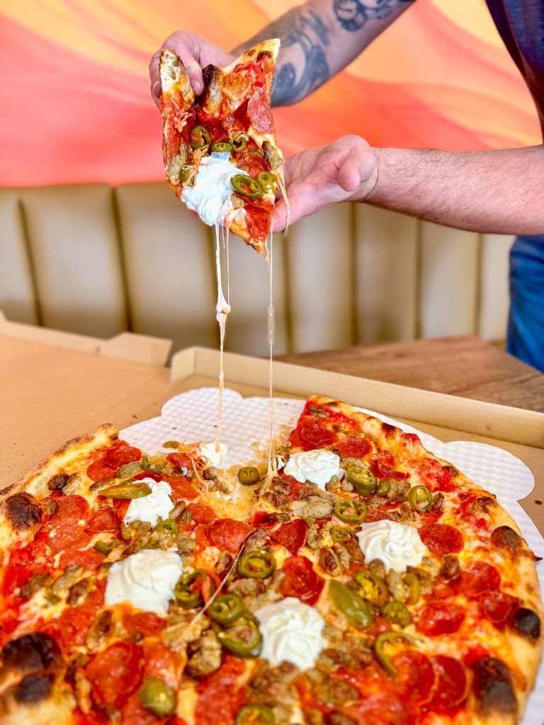 photo of a slice of pizza from Big Oven Pizza San Diego being pulled up in the air with melted cheese dripping down.